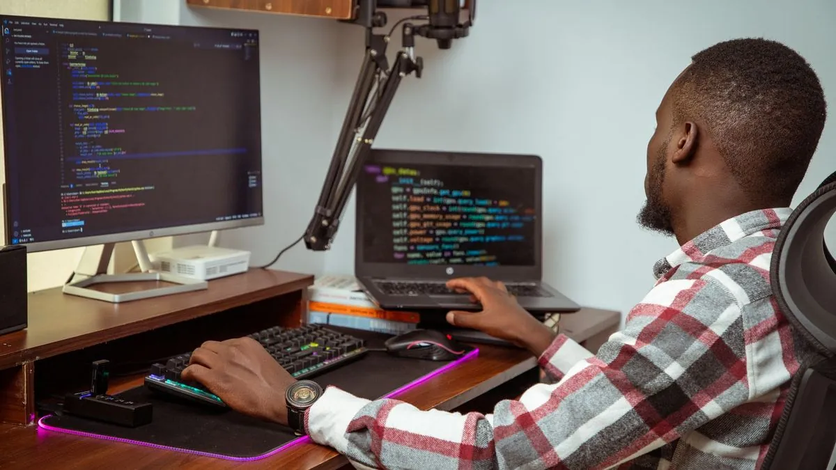 A developer writing code on a desktop and laptop screen